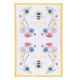 This white tea towel with a yellow rim surrounding its edges sports a design of bees and red, purple, yellow, and blue flowers and yellow text that reads "Bee Kind".