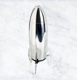 Looking down from the side on to a silver rocket shaped Cocktail Shaker standing up on a marble surface on it's three legs