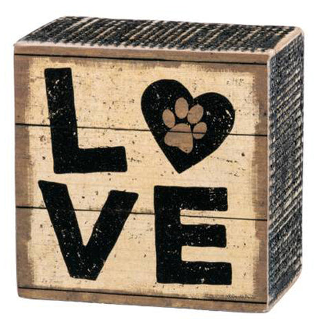 Rustic looking square, wood box sign with black capital letters 'L' and 'O' above the letters 'V' and 'E'. The "O" is the shape of a heart with a brown paw print in the center. The tan background and black ridged sides have a distressed painted look.