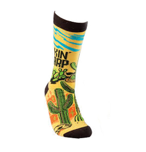 This yellow and orange sock with a black top, heel, and toe has a picture of a desert with green cactus and blue sky. Above the cactus are the words, "Lookin&