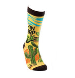 This yellow and orange sock with a black top, heel, and toe has a picture of a desert with green cactus and blue sky. Above the cactus are the words, "Lookin' Sharp" in black lettering.