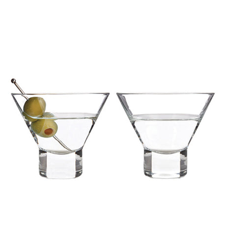 Two clear stemless martini glasses half full with a clear liquid, one has a cocktail pick with two green olives. The glasses are sitting next to each other on a white background.