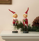 The two sculpted santa helper figurines are a boy and girl sitting on a mantle next to a wreath.