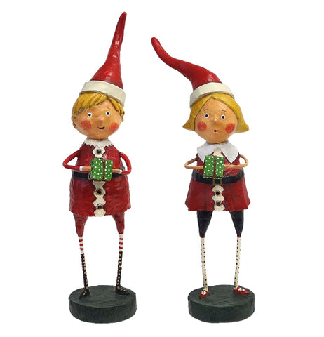 These sculpted figures are of a boy and girl dressed as Santa Claus helpers, wearing green and red clothes with santa hats and both holding presents wrapped in green with white polka dots.