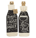 This black and white cloth wine bottle cover features the words, "Toast the Host with the Most" in white lettering on one side, and a picture of a hand raising a wine glass on the other.