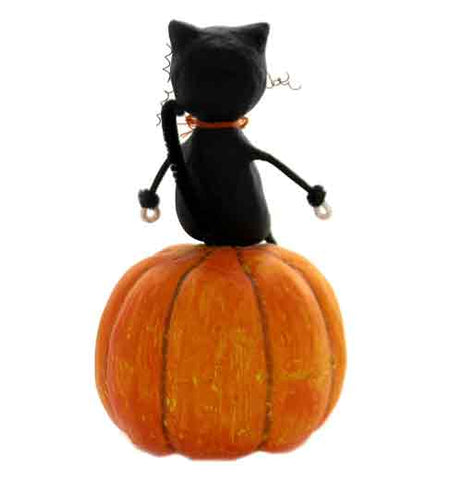 The figurine of a boy dressed in a cat costume sitting on a jack-o-lantern is shown from the rear.