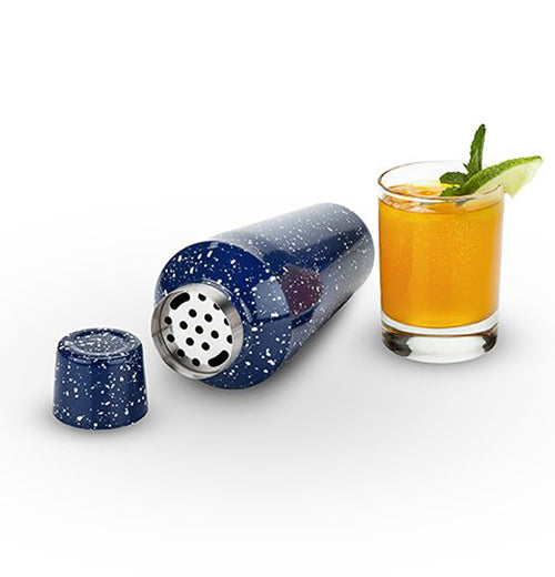 The Enamel Shaker is laying on its side and shows the strainer with the cap opened next to a glass of filled with the drink. 