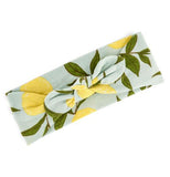 This light blue headband features yellow lemons with forrest green with the ends of the headband in a lightly knotted bow.