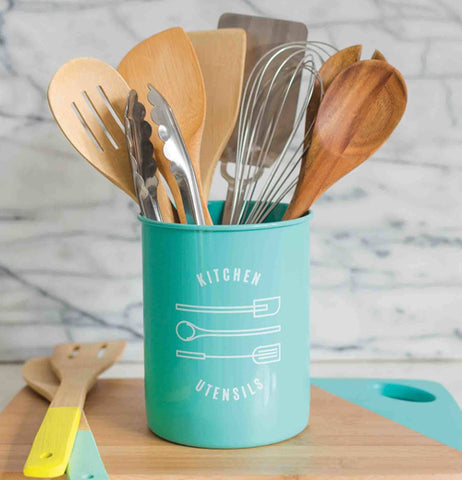  Some utensils are in a Metal powder-coated utensil crock with  two on a cutting board. 