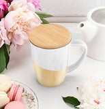 Gold Dipped tea mug with bamboo lid on table with flowers next to a white tea kettle and plate of sandwich cookies.