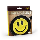 "Crack A Smile" pancake and egg mold in its box with scrambled eggs shaped like a smiling face in a black pan on a brown background.