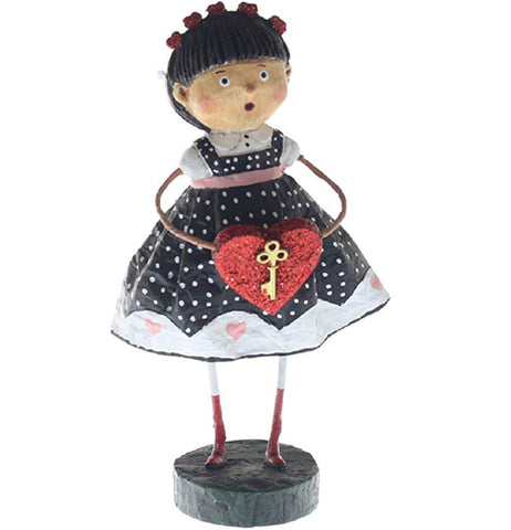 A resin figure of an olive-skinned girl. She is wearing a black dress with white polka dots, pastel pink hearts across the bottom, and a pastel pink ribbon across her chest. She is holding a red heart with a gold-painted key on it. She wears red socks and white leggings. She is standing on a black base.