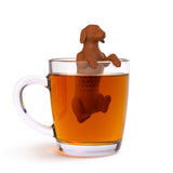 Red "Hot Dog" tea infuser perched in a clear glass tea mug with tea being brewed over a white background.