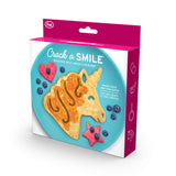 "Crack A Smile" mold box with unicorn head shaped pancake on a round blue plate with blueberries with red heart and star cookies.