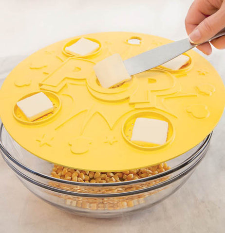 Microwave popcorn lid on top of a bowl of un popped popcorn with five pats of butter on top of lid.