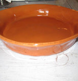 The oval-shaped orange baking dish is shown standing on a table.