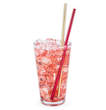 One red and one gold stainless steel cocktail straw in a clear pint glass filled with ice and a pink beverage.