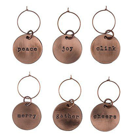 These six copper wine charms each have different words on them. The first says "Peace", the second says "Joy", the third says "Clink", the fourth says "Merry", the fifth says "Gather", and the sixth says "Cheers".