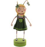 A polyresin figurine of a young, blonde-haired girl. She wears a green and gold painted four-leaf clover headband, a green dress with rainbow striped shirt underneath, white socks with two green stripes at the top, and Mary Jane shoes. She is facing the front.