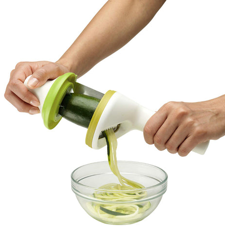 The zucchini is shown being cut and sliced into pasta noodle shapes by the slicer and deposited into a glass bowl.