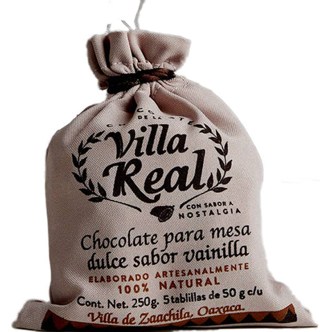 A white burlap bag presumably full of hot chocolate. Black text reads reads "Villa real chocolate," "100% natural," "Cont. Net. 250 G." and Villa de Zaachila, Oazaca." The rest of the text is in Spanish. The plant and geometric designs are black and red. It's tied up with a red rope.
