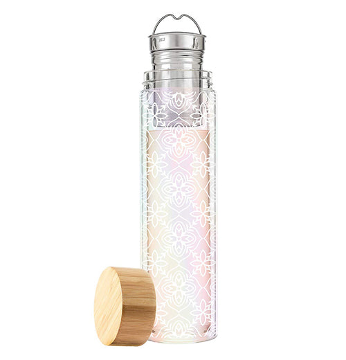 This tall glass with a crisscross pattern of white flower shapes has a metal tea infuser and strainer and a wooden lid lying next to it.