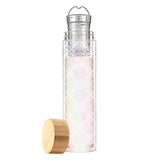 This tall glass with a crisscross pattern of white flower shapes has a metal tea infuser and strainer and a wooden lid lying next to it.