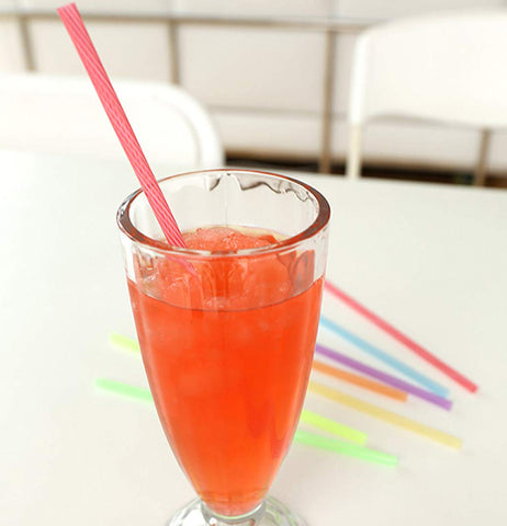 A pink reusable straw in a glass of punch with all the straws in the back ground.