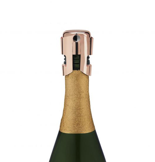 A bottle of champagne topped with a copper stopper above golden paper on a black bottle. 