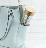 The glass tea mug is shown sticking out the pocket of a purse.