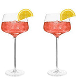 Two Glasses with long stems and short squat cups filled with ice, pink liquid and lemon wedges placed on the side. 
