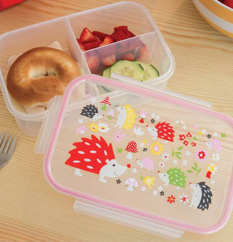 The lunch box with the porcupine design lid is shown with a bagel and some fruit inside it.