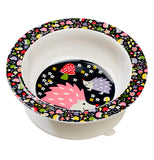 This white bowl with a black rim and bottom features a design of yellow, red, periwinkle, and green flowers on its rim, and a pink and periwinkle hedgehog pair on the bottom standing in front of a red and green mushroom.