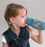 A little girl in a blue coat and pigtails is shown drinking from the blue water bottle.