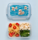 A closed plastic clear and blue bento box with otter decor sits above an open bento that has spaghetti noodles with grape tomatos in the biggest compartment, popcorn in the smaller compartment, and lettuce in the other smaller compartment.