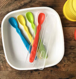 The set of four Infant Spoons were set in the bowl on the table. The red spoon sits in the open clear case. 