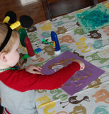 A little boy is shown doing artwork using the numbered animal splat mat as cover for the table.