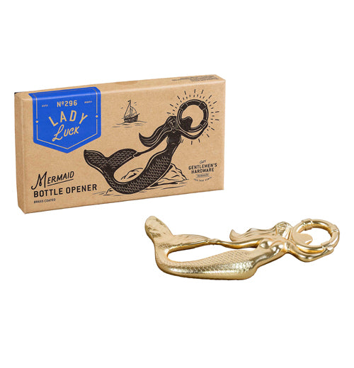 A brown box with a blue ribbon and a black picture of a mermaid and a sailboat are shown. On the blue ribbon are the words, "Lady Luck" in white lettering. At the bottom of the box next to the mermaid are the words, "Mermaid Bottle Opener" in black lettering. The brass mermaid bottle opener is shown beneath the box.