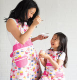 A mother and daughter are both shown wearing the pink aprons with the different colored cupcakes covering them.