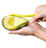 A hand is holding a green avocado slicer thats slicing an avocado.