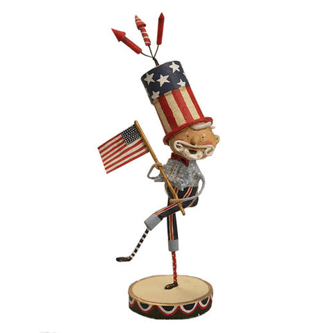 This figurine is of a man with a white beard dressed in light and dark blue holding the American flag and wearing a top hat with an American flag design on it. Three fireworks rockets are shown at the top of the hat.