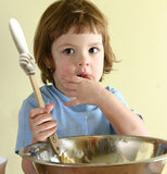 Girl holding the batter finger spatula over a mixing bowl while eating what's in the bowl
