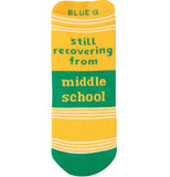 yellow sock with green toes there are white stripes segmenting the sock at the toes about an inch up form the toes and at the top of the sock. the words "Still recovering from middle school" with the middle school part being inside 