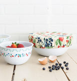 The strawberry and blueberry designed cloth top is shown covering a white bowl on a table.
