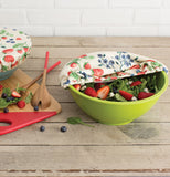 The cloth cover with the strawberry and blueberry design is shown half open on a bowl full of strawberries.