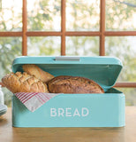 Turquoise Bread Box filled with different kinds of bread and sitting on a wood counter with a glass paneled window in the background.