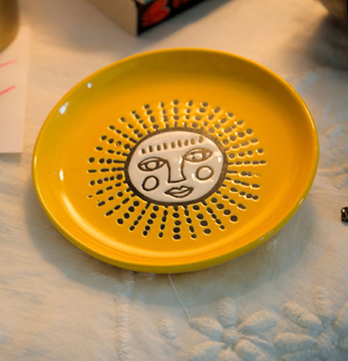 The yellow coaster with the white faced sun is shown sitting on a white table cloth.