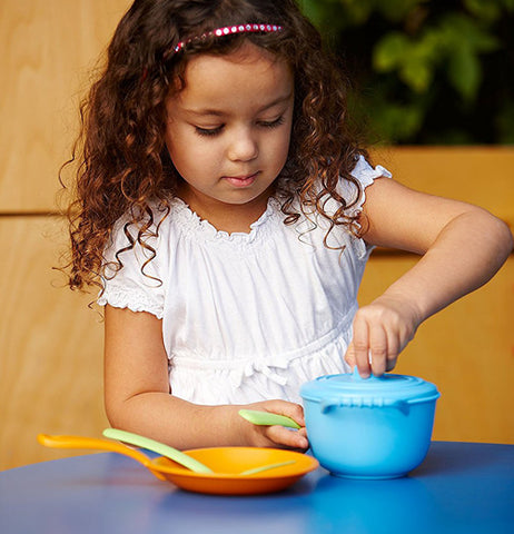 little girl playing with the blue pot and skillet with the yellow spatula