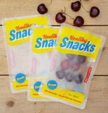 Three bags are shown lying on a wooden table. Two of them are empty. The third is seen holding some cherries in it. Some cherries are also shown sitting on the wooden table above the bags.