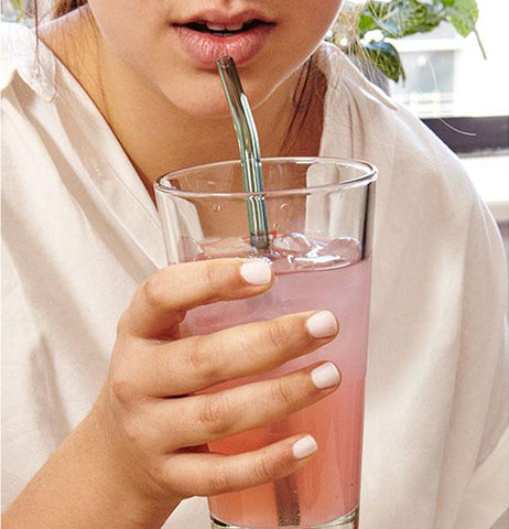 A woman is shown drinking lemonade from a glass with the curved green straw.